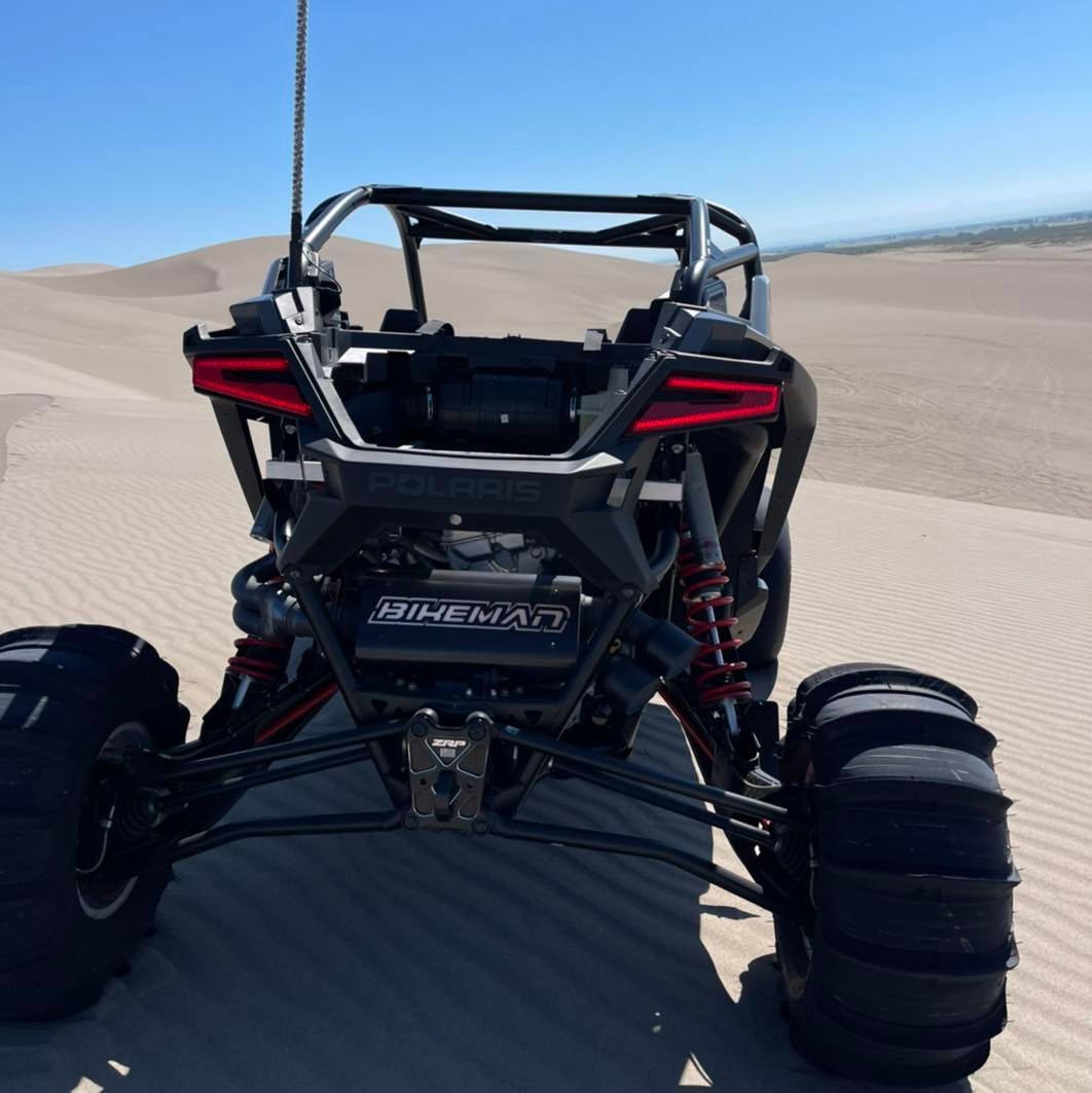 bikeman performance pro r slip on exhaust in black with raw accent installed on machine in the dunes 