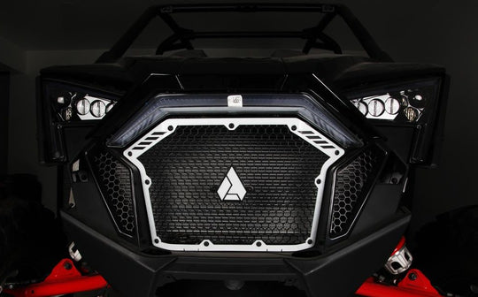Assault Industries Stinger Grill installed on a Polaris RZR Pro XP featuring black honeycomb mesh and white trim, with LED lights on the sides.