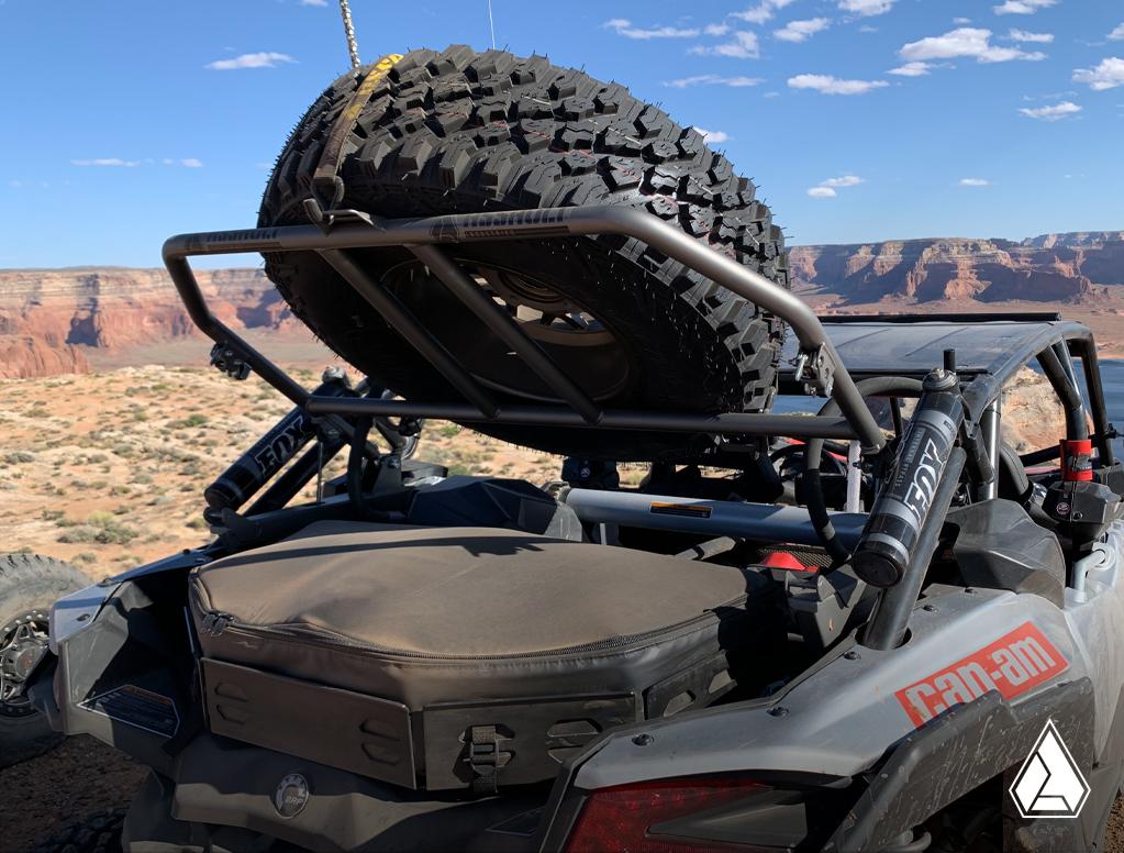 Can-Am Maverick X3 equipped with Assault Industries Adventure Rack X (ARX) holding a spare tire, showcasing the utility upgrade in a desert landscape.
